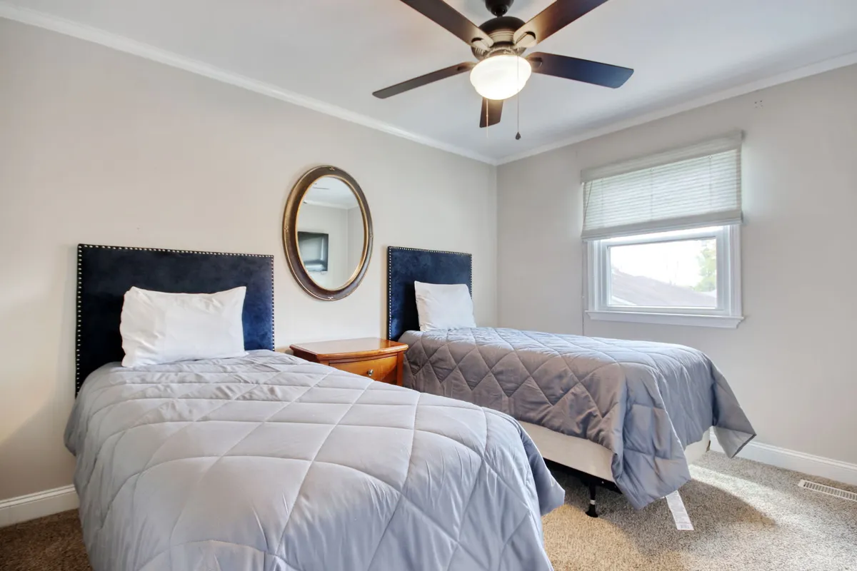 A tranquil bedroom with two twin beds, a wooden nightstand, and a round mirror. Sunlight softly fills the space, and the room is arranged for both comfort and peaceful late-night conversations.