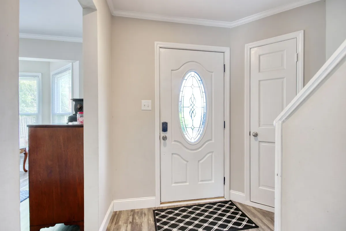 This image captures the home's front entryway, featuring an inviting doormat, wooden furniture, and a view of the staircase. The space feels open and welcoming, suggesting a comfortable return after a day out.